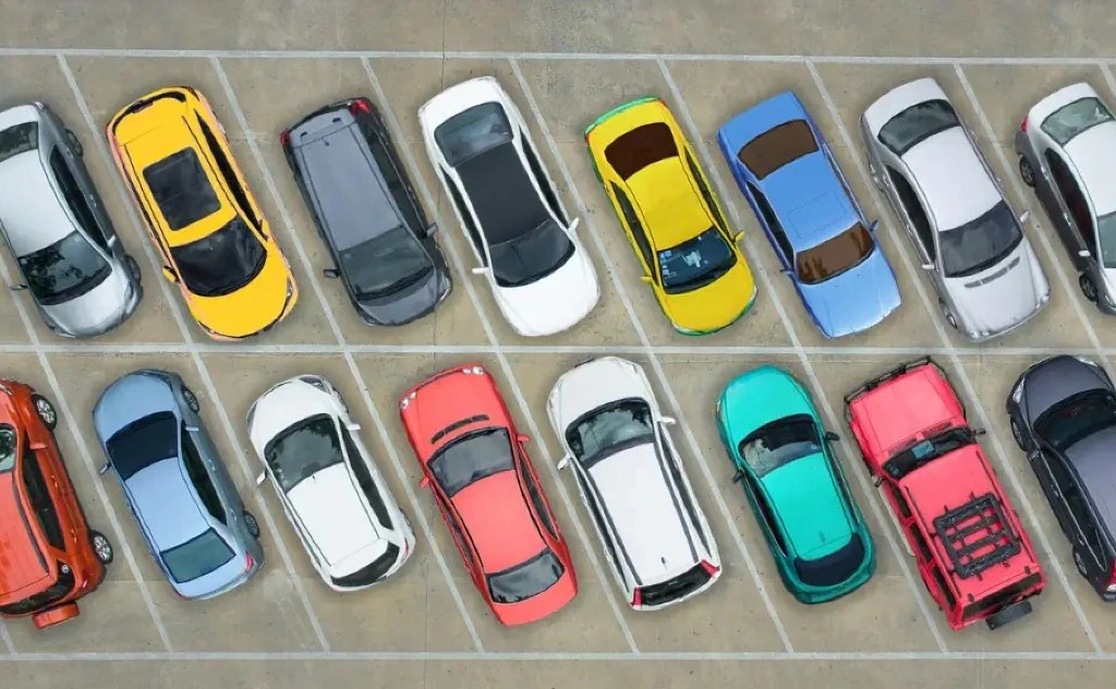 Vue aérienne d’un parking : deux rangées de berlines, citadines et SUV colorés sur emplacements marqués de lignes blanches — flotte d’entreprise