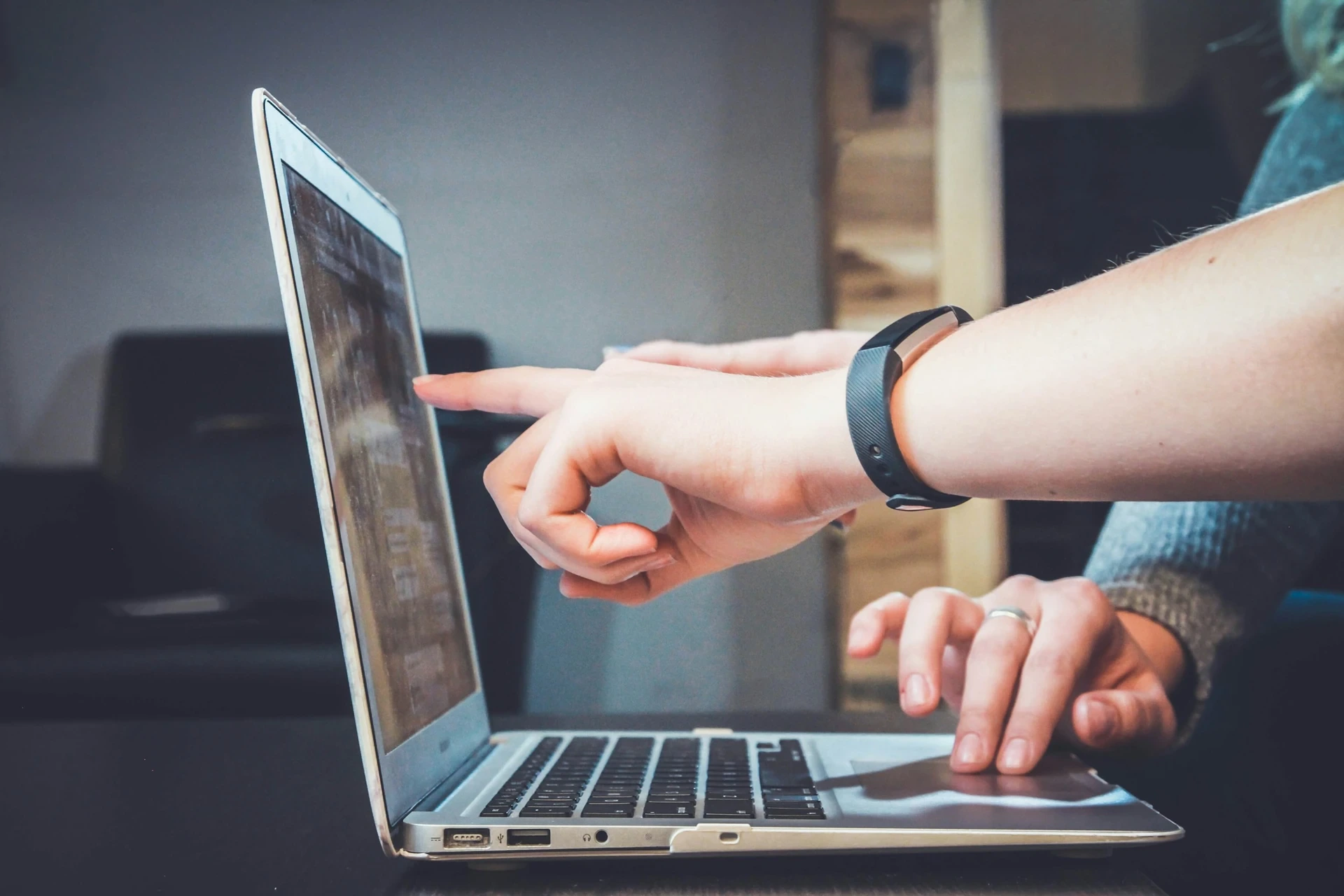 Gros plan sur deux mains près d’un ordinateur portable : une personne pointe l’écran, l’autre utilise le pavé tactile — collaboration et soutien professionnel