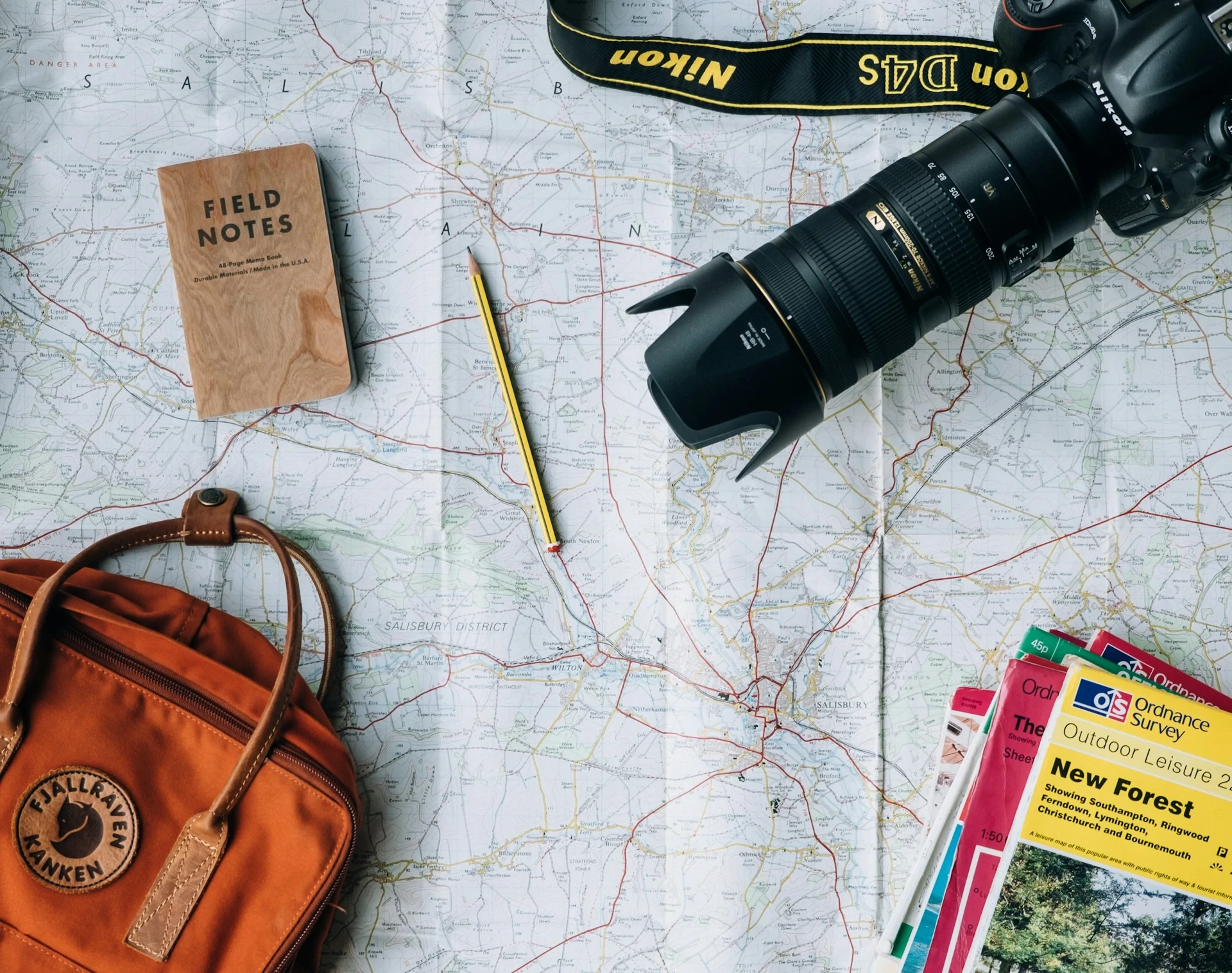 Vue du dessus : carte topographique dépliée, petit carnet, appareil photo reflex et guides outdoor — mobilité internationale et couverture santé à l’étranger